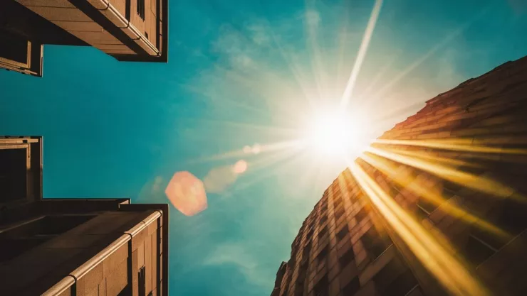 Una foto de un cielo azul donde el sol brilla de manera prominente, proyectando una luz dorada que se refleja en los edificios