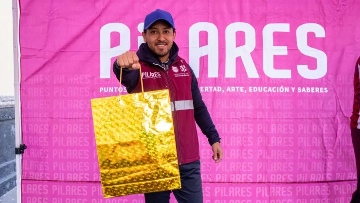 Uno de los talleristas de PILARES con una bolsa de regalo dorada en alusión a las nuevas vacantes.