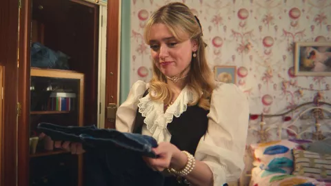 Aimee Lou Wood mirando unos pantalones en su papel de Sex Education, serie de Netflix