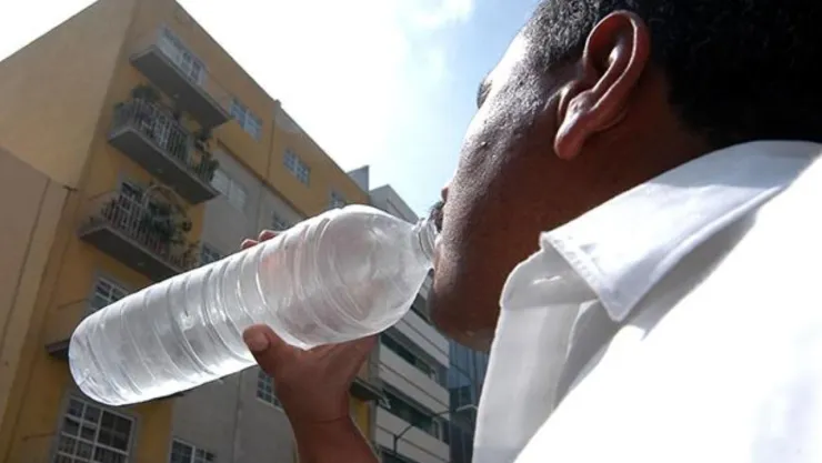 Un hombre tomando agua ante el imponente rayo del sol.