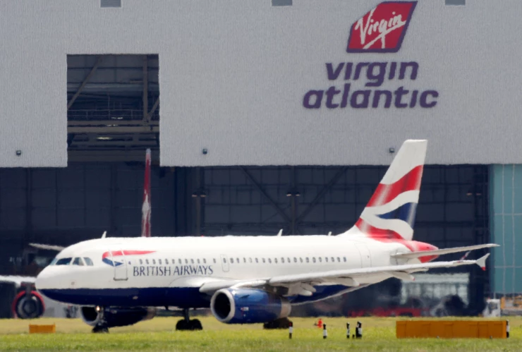 FILE PHOTO: A British Airways aeroplane is seen through a heat haze in front of a Virgin Atlantic hanger at London’s Heathrow airport
