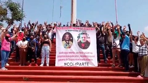 Personas alzando los brazos sosteniendo un cartel en un manifestación en Comitán.