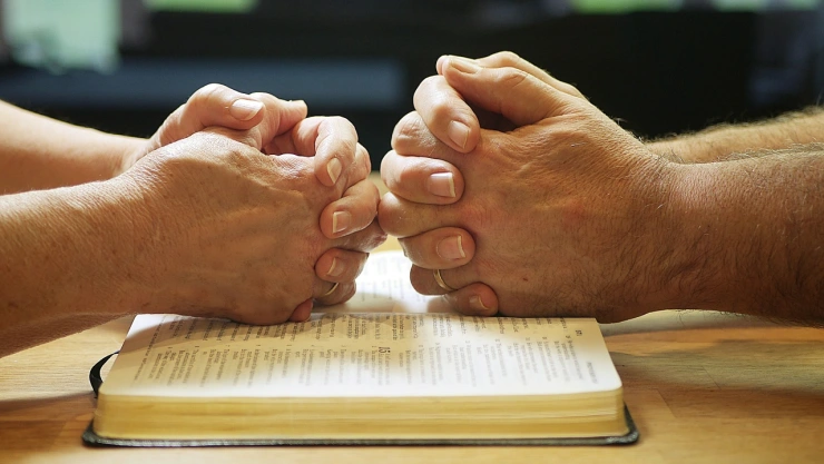 Foto de dos personas orando sobre Biblia.