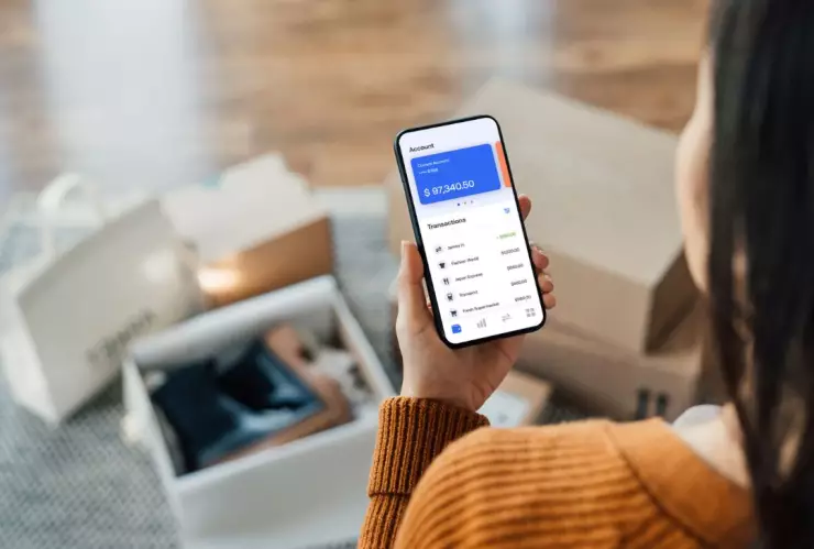 Mujer sosteniendo un teléfono y rodeada de cajas con productos