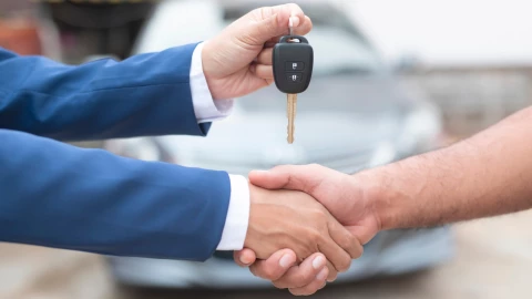 Las manos de dos personas estrechándose tras un acuerdo mientras muestran una llave de coche.