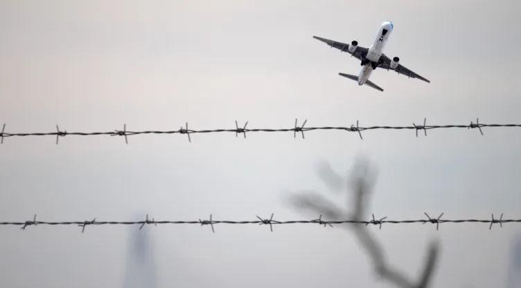Vista de un avión despegando frente a una valla con alambre de púas.