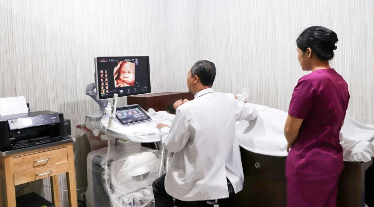 Consultorio de ginecólogo con paciente y enfermera realizando un ultrasonido.