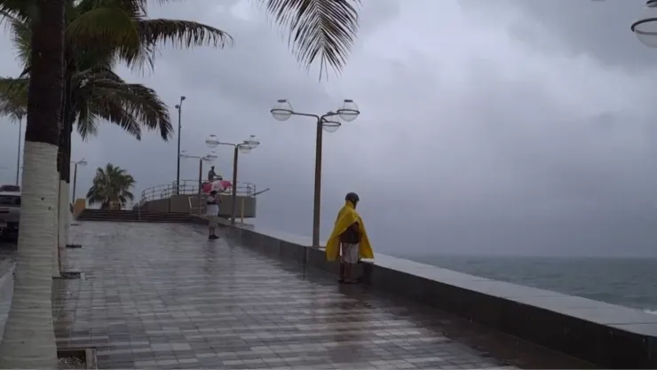 Hombre con impermeable parado bajo la lluvia, en el Malecón de Mazatlán