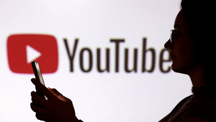 FOTO DE ARCHIVO: Un adolescente posa para una foto mientras sostiene un teléfono inteligente frente a un logotipo de YouTube en esta ilustración tomada el 11 de septiembre de 2025.