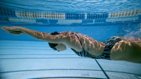 Nadadora realizando apnea después del salto en piscina.