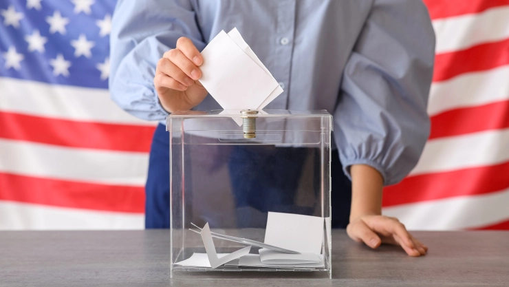 Mujer coloca su voto junto al resto con la bandera estadounidense en el fondo