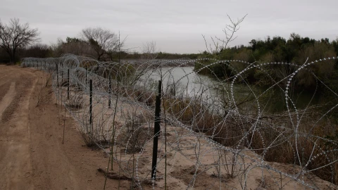 Alambre de púas que separa un territorio de tierra de otro con un río