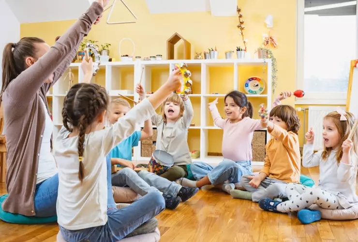 Una maestra y sus alumnos forman un círculo y alzan las manos