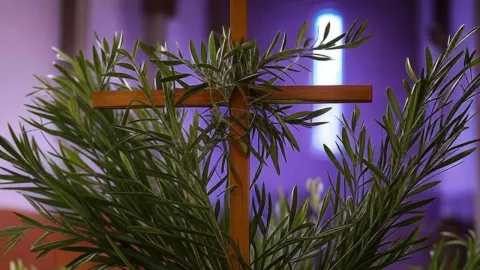 (Imagen generada con IA) Ramos de olivo con un fondo morado de fondo y una cruz para representar el Domingo de Ramos 2025.