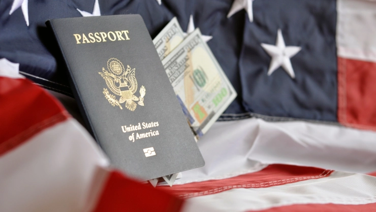Un pasaporte estadounidense sobre una bandera y billetes de 100 dólares.