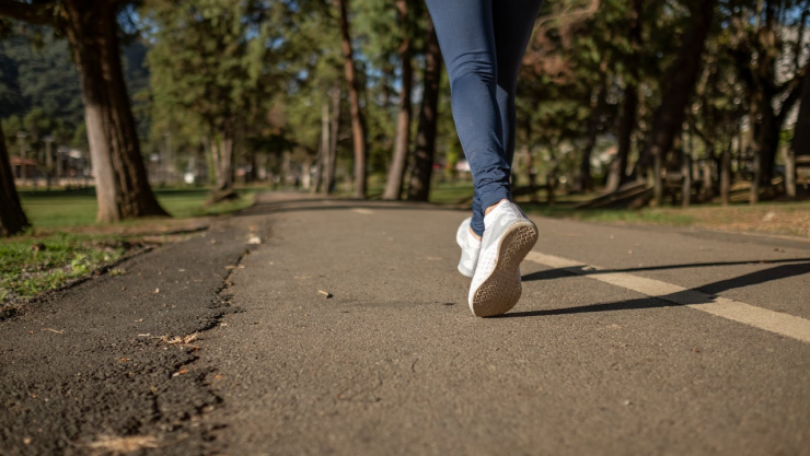 Persona con jeans azules y tenis blancos caminando por la carretera.
