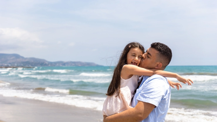 Un padre besa a su hija en brazos en una playa