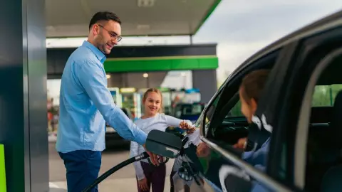 un hombre carga combustible junto a sus ni&ntilde;as