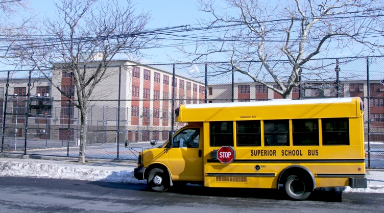 Un bus escolar amarillo, estacionado afuera de la escuela en Nueva York, en invierno, con las veredas nevadas