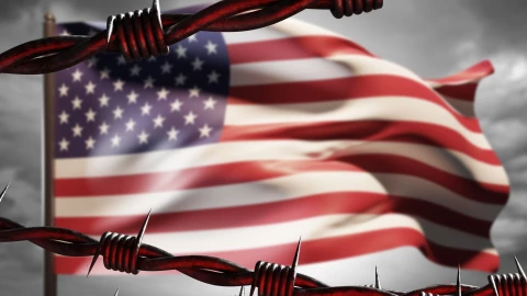 Una bandera estadounidense tras un muro de alambre.