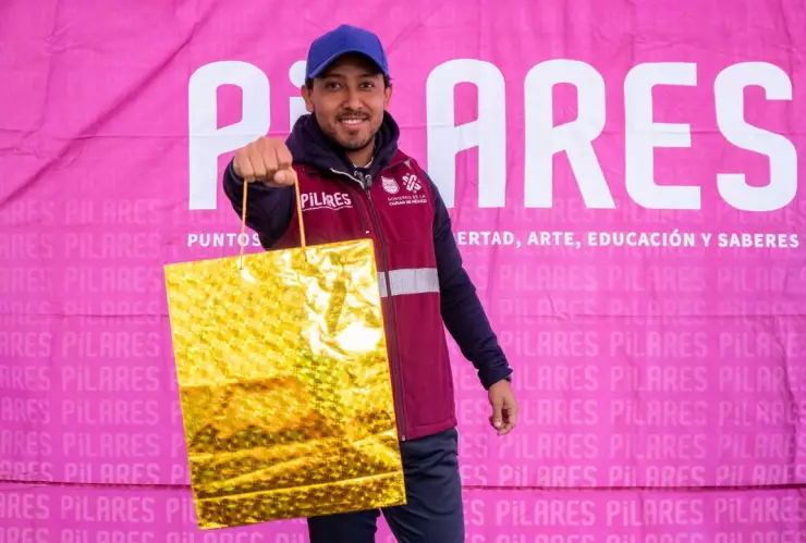 Uno de los talleristas de PILARES con una bolsa de regalo dorada en alusión a las nuevas vacantes.