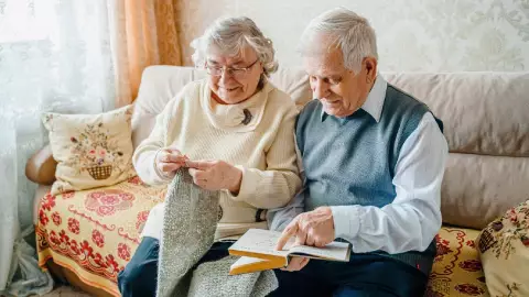 Una pareja de jubilados felices leen y tejen