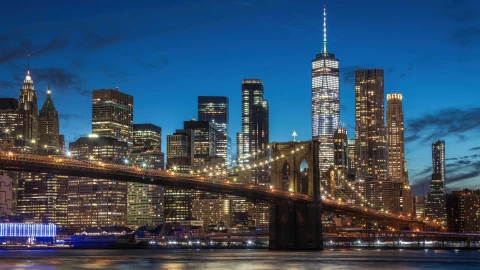 El puente Brooklyn y la ciudad de Nueva York a lo lejos en el anochecer, con los edificios y sus luces encendidas