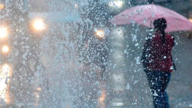 Mujer bajo la lluvia con un paraguas de color rosa.