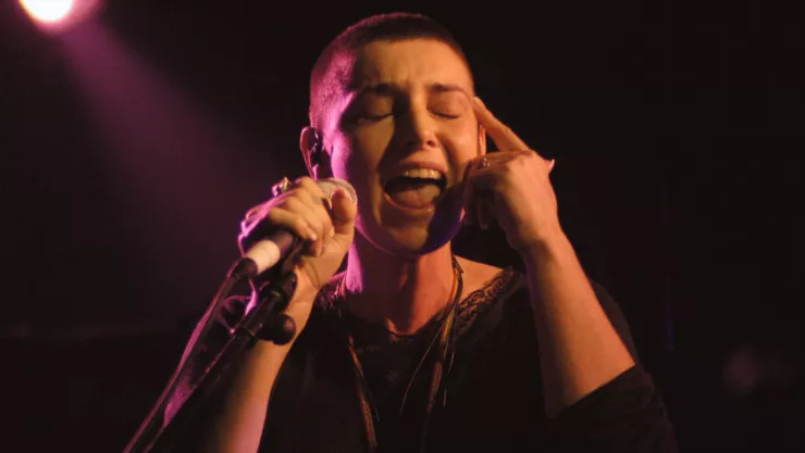 Sinead O’Connor con la cabeza rapada, un micrófono en la mano y cerrando los ojos cantando una canción