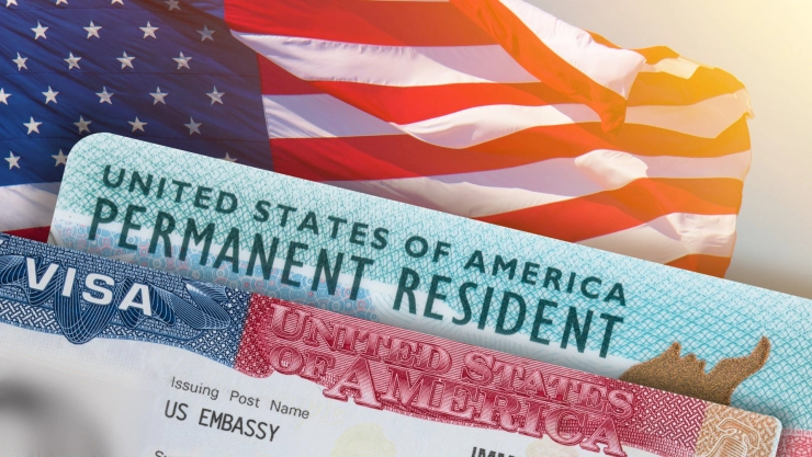Una Green Card y una visa estadounidense sobre una bandera.