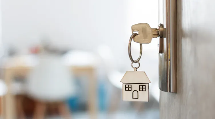 Una llave introducida en la puerta con un llavero de una casa