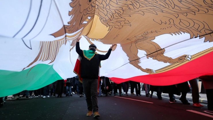 Persona camina con bandera de Irán encima en protesta en Londres, Inglaterra.