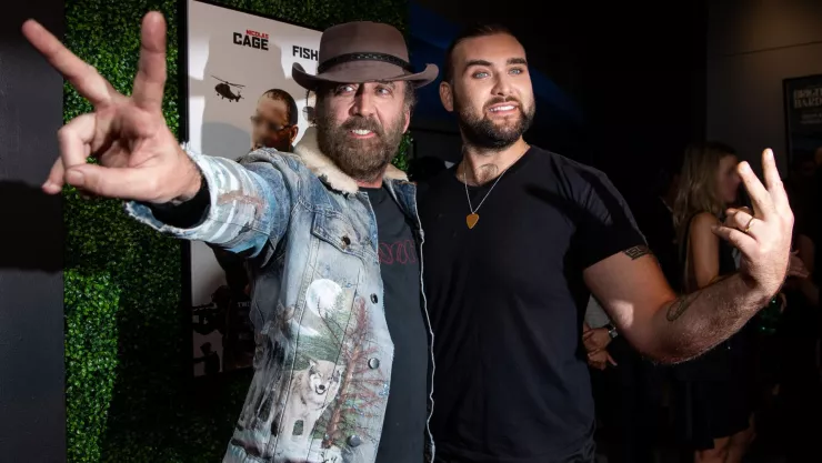 Están Weston Cage y Nicolas Cage sonriendo y haciendo el símbolo de paz con las manos en la presentación de una película