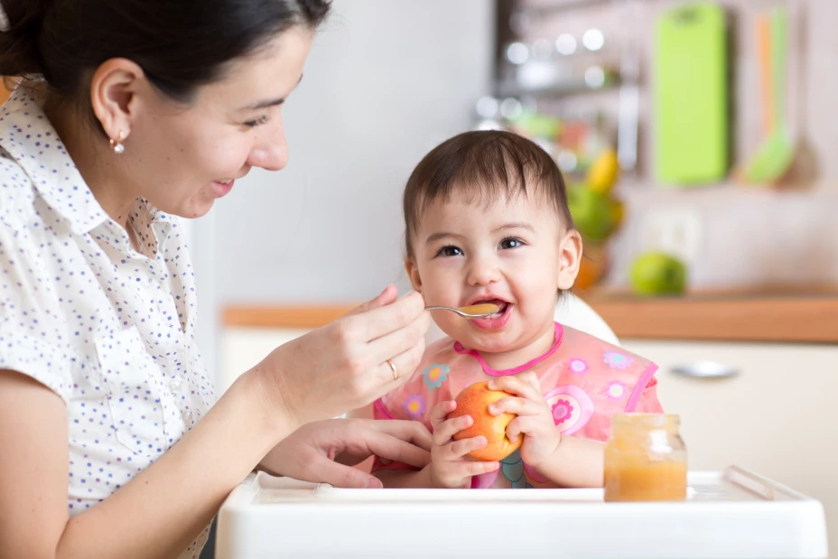 baby child sitting in chair with a spoon and eating healthy food
