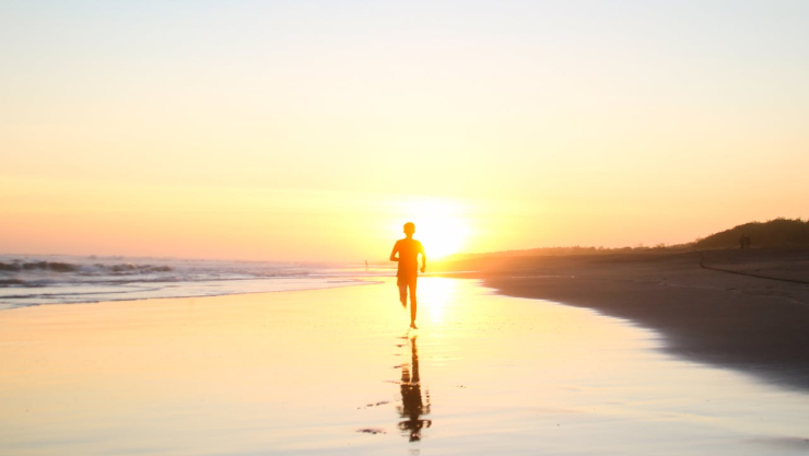 Hombre corriendo frente a la puesta de sol en la playa.