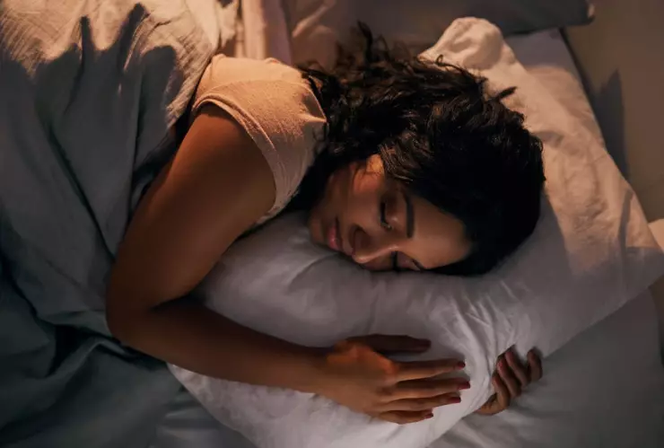 mujer durmiendo sobre su costado y abrazando una almohada