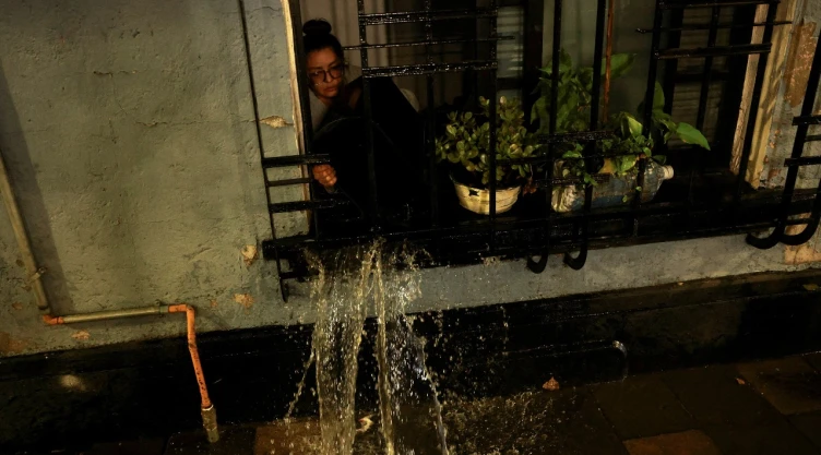 Una mujer retira el agua que inundó su departamento a través de una ventana que da a la calle, luego de fuertes lluvias en la Ciudad de México el 10 de agosto de 2025.