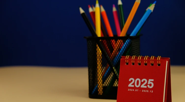 Un calendario escolar del 2025 junto a un conjunto de lápices de colores.
