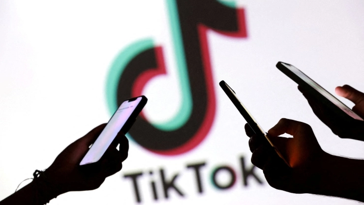 Logo de TikTok detrás de manos con celulares.