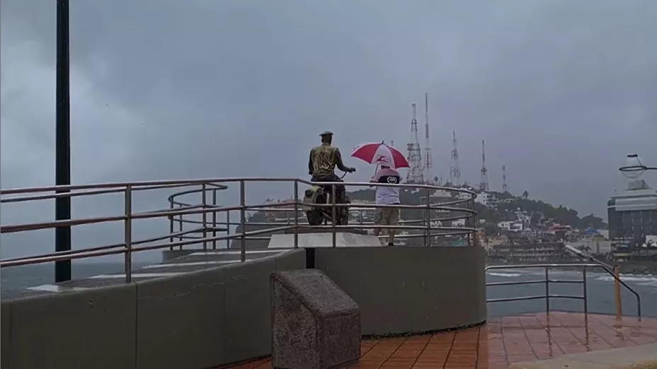 Hombre con paraguas bajo la lluvia, junto al monumento a Pedro Infante en el malecón de Mazatlán
