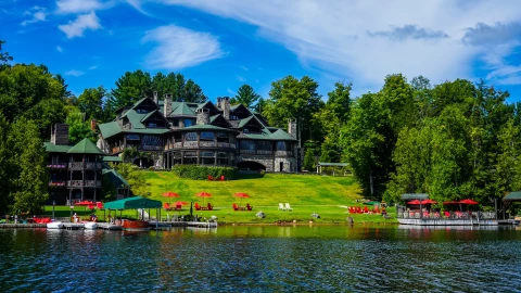 Casa rústica a la vera del lago, rodeada de grandes árboles verdes y botes a la vera de la superficie terrestre.