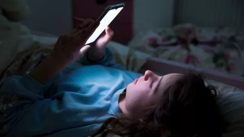 Una niña revisa un teléfono en su cama.