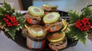 Siete frascos con tapas doradas que contienen salsas hechas en méxico y están colocados en una canasta con adornos tipo navideños