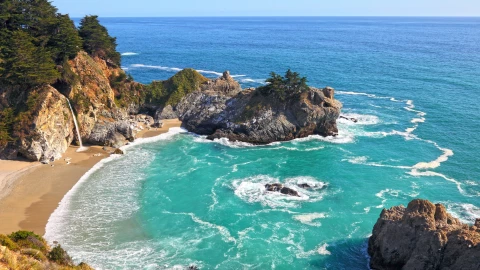 Vista aérea de luna pequeña playa rodeada de rocas y vegetación con el agua color turquesa