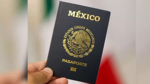 Un pasaporte mexicano siendo sostenido con una mano frente a una bandera de México desenfocada