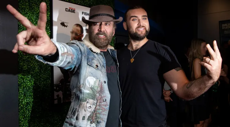 Están Weston Cage y Nicolas Cage sonriendo y haciendo el símbolo de paz con las manos en la presentación de una película