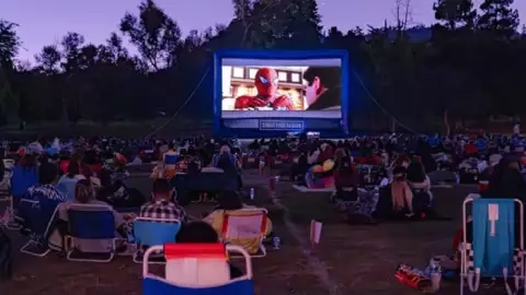 un grupo de cinéfilos reunidos a aire libre viendo Spider-Man.