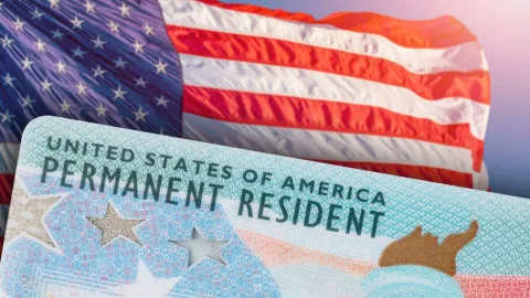 Una Green Card junto a una bandera de Estados Unidos.