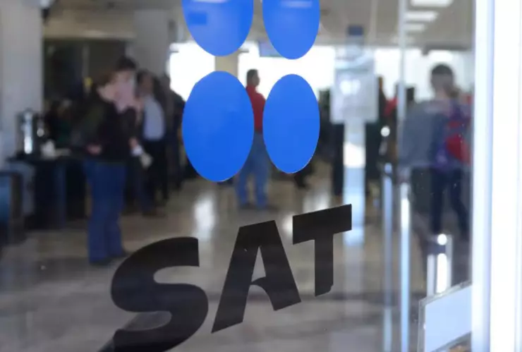 Puerta de cristal en las oficinas del SAT con el logo de la institución, en el fondo se ven varias personas