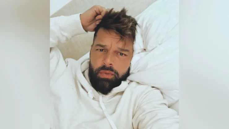 En la foto se ve a Ricky Martin vestido de blanco acostado en una cama con sabanas blancas